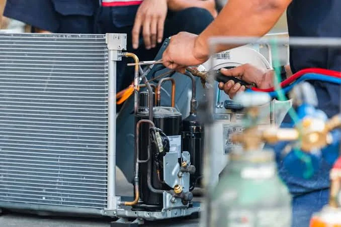 Technicians working on the refrigerant piping and components of an air conditioner