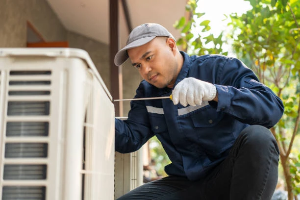 Technician inspecting an outdoor air conditioning unit beside a home